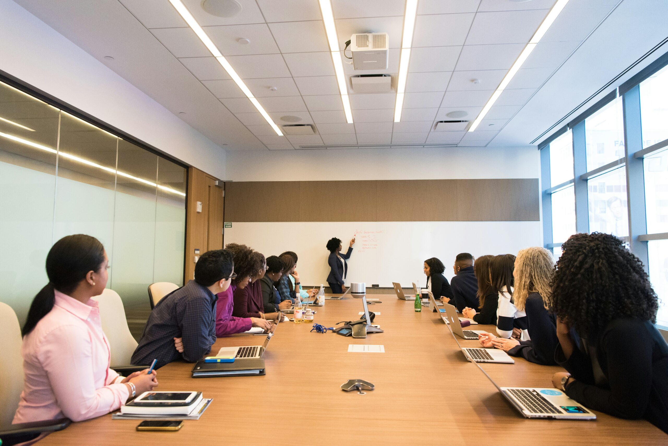 Group of professionals sitting in a modern conference room, engaging in a presentation with laptops and notebooks.